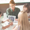 Positive teacher and children creating toy Satisfied kid playing with contemporary robot. Beaming lady and friends looking at her in classroom. Modern digital device concept